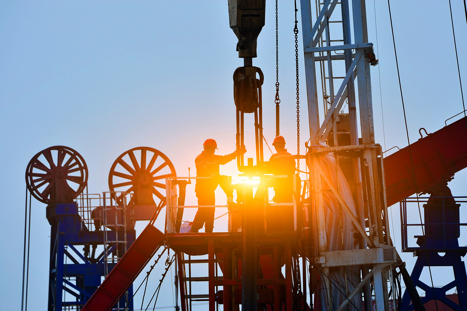 Two oil rig workers in hard hats operating drilling equipment at sunrise